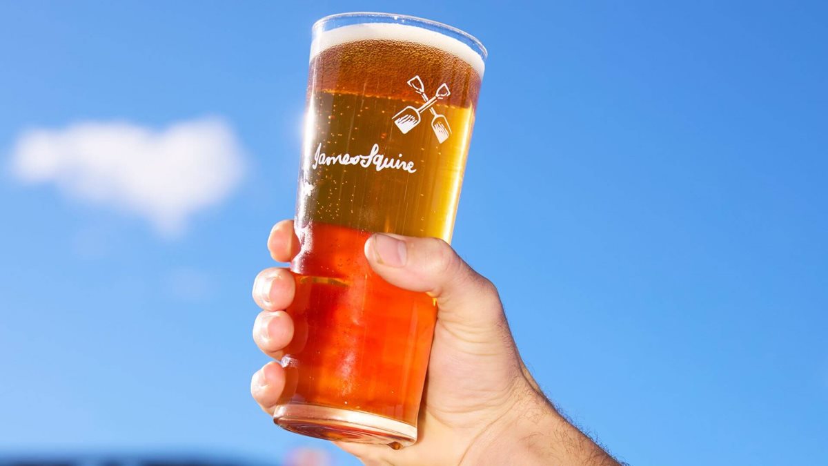 James Squire beer raised against a blue sky